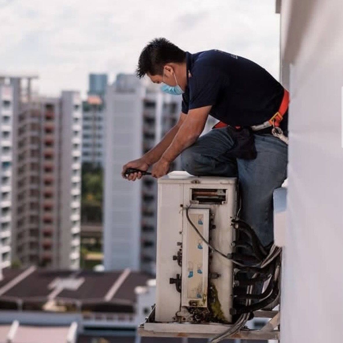 JW technician in safety harness servicing a condenser unit on an HDB ledge